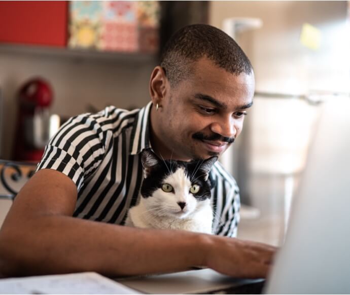Mand bruger bærbar computer, mens han holder en kat