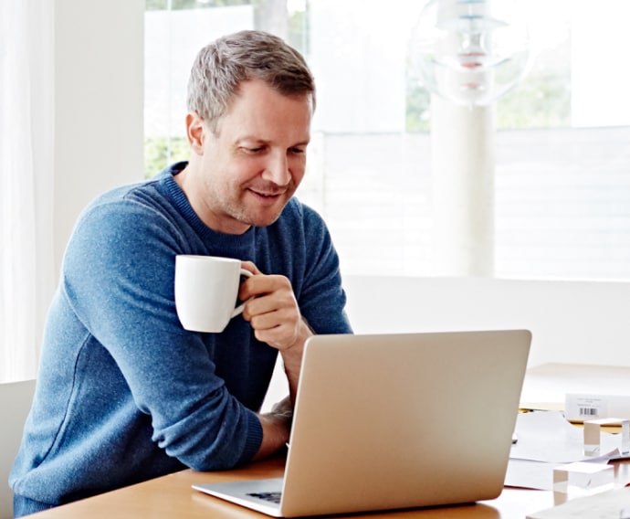 Mand derhjemme, der bruger en bærbar computer og drikker kaffe.