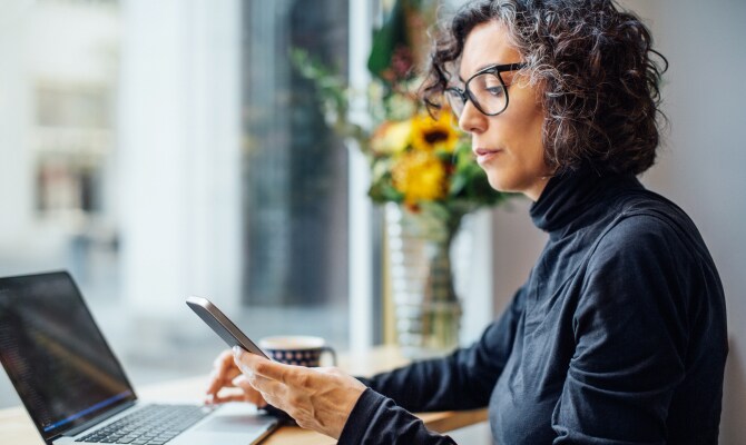 Kvinde kigger på en mobiltelefon foran en laptop